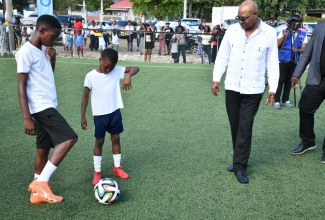 Tourism Minister, Hon. Edmund Bartlett, observes as young football players test out the new futsal court in Nannyville, St. Andrew, during the facility