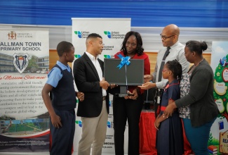 Deputy General Manager for Corporate Services, Urban Development Corporation (UDC), Adrian Chin (second left), presents computer equipment to Acting Principal of the Allman Town Primary School, Thamar Russell-Brown (third left), during Read Across Jamaica day activities at the school in Kingston on May 5.  Joining in the occasion (from left) are male student leader, Yajaun Ainsworth;  Education Officer, Lucien Henry;  female student leader, Tashayne Johnson, and School Board Chairman, Renee Campbell. 
