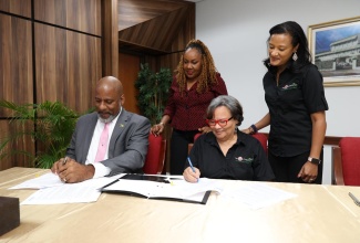 Planning Institute of Jamaica (PIOJ) Director General, Dr. Wayne Henry (seated left), and Founder of Honey Bun Foundation, Michelle Chong (seated right), affix their signatures to a Memorandum of Understanding (MOU) to undertake a micro enterprise business development and growth monitoring initiative. The MOU signing ceremony was held at PIOJ’s Oxford Road offices in Kingston on Thursday (April 30). Observing the signing (from left) are PIOJ Technical Specialist: Socio-Economic Development, Charmaine Brimm; and General Manager of Honey Bun Foundation, Nashauna Lalah.
