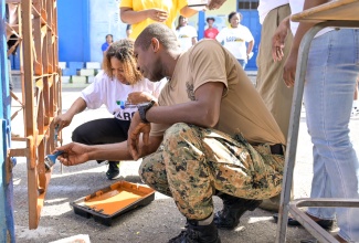 Minister of Education, Skills, Youth and Information, Dr. the Hon. Dana Morris Dixon (left), is joined by Major Phillip Edwards of the Jamaica Defence Force (JDF) in painting a grill, during Labour Day activities at St. Anne