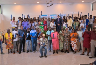 Prime Minister, Dr. the Most Hon. Andrew Holness (centre, in suit); Minister without Portfolio in the Ministry of Economic Growth and Infrastructure Development, with responsibility for Land Titling and Settlements, Robert Montague (seventh right), and other officials pictured with some of the 124 residents in Manchester, who received land titles from the National Land Agency (NLA), during a ceremony held at the Garden Hotel in Mandeville, on May 27