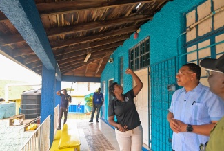  Prime Minister, Dr. the Most Hon. Andrew Holness (centre) and Minister of Local Government and Community Development, Hon. Desmond McKenzie (right) listen to Principal, Voluntary Organisation for Uplifting Children (VOUCH) Sylvia Foote Basic School, Kaleela Williams Bromfield, as she shows the roof at the school on Friday (May 30).