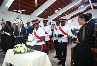 Marlene Malahoo Forte (right), Member of Parliament for St. James West Central and widow of the retired Court of Appeal President, Justice Ian Forte, in deep reflection as members of the Jamaica Constabulary Force (JCF) escort the urn bearing the eminent jurist