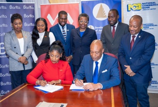 Development Bank of Jamaica (DBJ) Managing Director, Dr. David Lowe (right, seated), and Victoria Mutual (VM) Assistant Vice President – Lending Solutions and Business Services, Latoya Williams (left, seated), sign the Approved Financial Institutions (AFIs) agreement. Looking on are executives from DBJ and VM. The signing took place during the M5 Business Recovery Programme Additional Partner Commitment Ceremony, held on Wednesday (June 24) at the DBJ’s offices on Oxford Road in Kingston.
