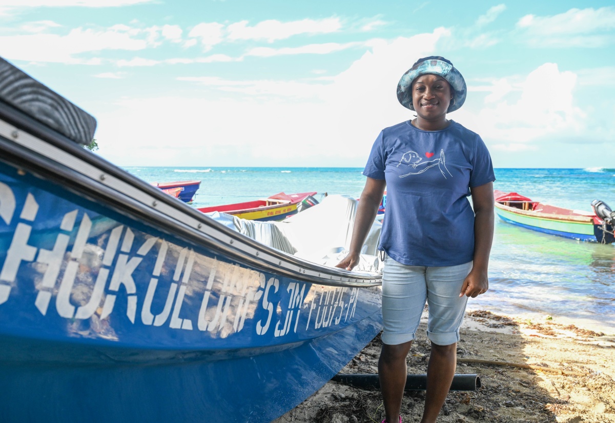 Female fisher, Shashay Shaw, stands proudly beside the 26‑foot single‑engine boat she received through the Fisheries Production Incentive Programme.
