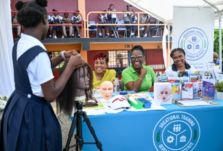 Vocational Training Development Institute (VTDI) team members (seated from left) Beauty Services Lecturer, Stacy-Ann Robinson-Panton; Communication and Marketing Manager, Shieka Walsh; and Social Media and Marketing Officer, Kendra Tulloch Miller, look on as a student from St. Thomas Technical High School displays her hairstyling skills. Occasion was a Triple Impact Day at the school recently.
