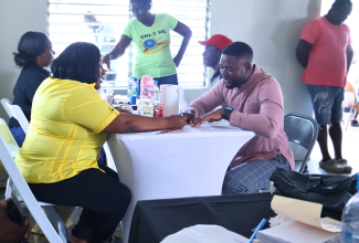 Mayor of Montego Bay, Councillor Richard Vernon, (right, seated), engages with Customer Service Manager at the Passport, Immigration and Citizenship Agency (PICA), Emoy Henry Tingling, during a job fair and document drive hosted at the Rose Heights Community Centre in St. James on June 4
