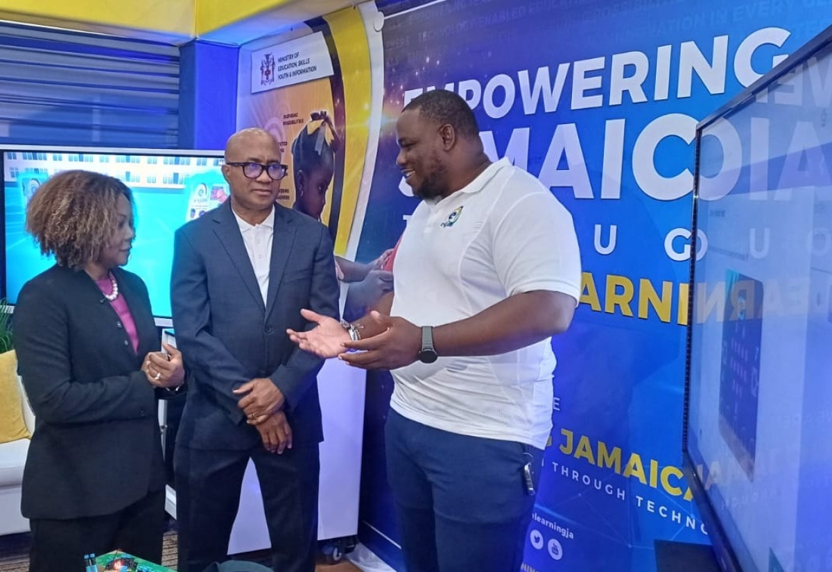 Minister of Education, Skills, Youth and Information, Senator Dr. the Hon. Dana Morris Dixon (left) listens to Regional Training Officer of e-Learning Jamaica, Garfield Morrison (right),as he gives an update on current e-Learning projects. Occasion was a tour by the Minister of booths at the 11th Biennial Jamaica Diaspora Conference on Tuesday (June 16) at the Montego Bay Convention Centre in St. James. Looking on is Chief Executive Officer of e - Learning , Andrew Lee.