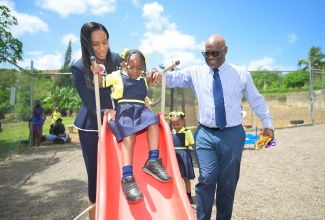 State Minister for Education, Skills, Youth and Information, Hon. Rhoda Moy Crawford (left) and Board Chairman, Devon Primary and Infant School, Glenroy Griffiths, assist Karissa Sparkes down a slide in the new playground at the institution. The facility was officially opened on Monday (Sept. 14) as part of activities for the ceremonial opening of schools. 