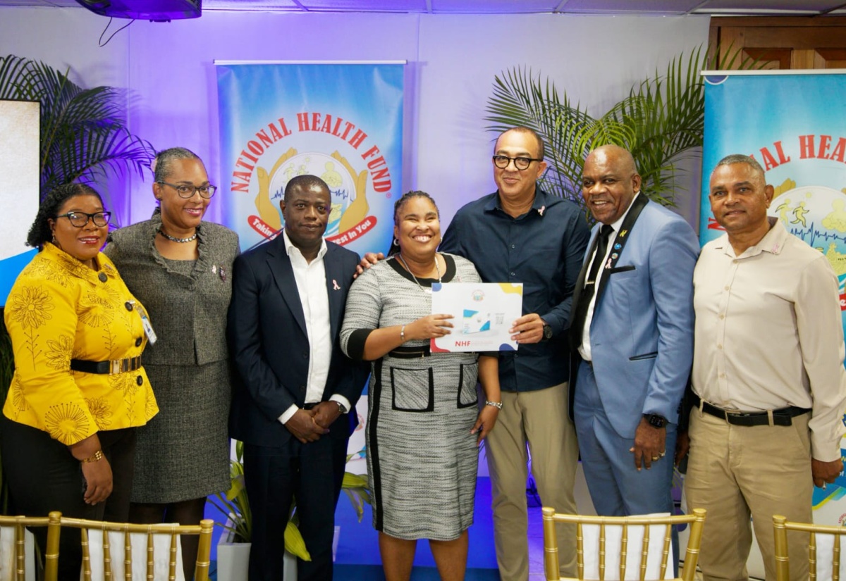 Minister of Health and Wellness, Dr. the Hon. Christopher Tufton (third right), hands over an updated NHF Card to Kimiela Isaacs (centre), at the official launch of the Double Subsidy Benefit for Persons with Disabilities at the National Health Fund (NHF) head office in New Kingston on October 15. They are joined by (from left) Acting Executive Director of the Jamaica Council for Persons with Disabilities, Desreen Boothe; NHF Board Member, Dr. Kamal Mars; Chief Executive Officer, NHF, Everton Anderson; Director of the UWI Centre for Disability Studies, Professor Floyd Morris and Deputy Chairman of the NHF Board, Michael Stern. 
