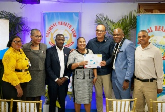 Minister of Health and Wellness, Dr. the Hon. Christopher Tufton (third right), hands over an updated NHF Card to Kimiela Isaacs (centre), at the official launch of the Double Subsidy Benefit for Persons with Disabilities at the National Health Fund (NHF) head office in New Kingston on October 15. They are joined by (from left) Acting Executive Director of the Jamaica Council for Persons with Disabilities, Desreen Boothe; NHF Board Member, Dr. Kamal Mars; Chief Executive Officer, NHF, Everton Anderson; Director of the UWI Centre for Disability Studies, Professor Floyd Morris and Deputy Chairman of the NHF Board, Michael Stern. 
