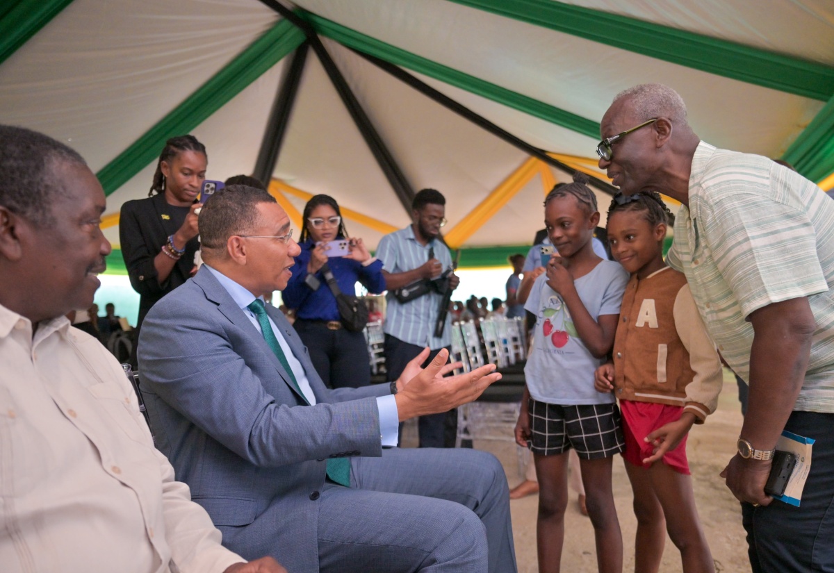 Prime Minister, Dr. the Most Hon. Andrew Holness (second left), greets young Tivoli Gardens residents Cathalia Collins (centre) and Mourica Rose, during the Certificate of Possession Handover Ceremony held at the Tivoli Gardens Community Centre in Western Kingston on Wednesday (October 14). Looking on are Minister without Portfolio in the Ministry of Economic Growth and Infrastructure Development with responsibility for Land Titling and Settlements, Hon. Robert Montague (left), and Minister of Local Government and Community Development and Member of Parliament for Western Kingston, Hon. Desmond McKenzie (right). Approximately 221 Tivoli Gardens residents received Certificates of Possession, bringing them one step closer to full homeownership.
