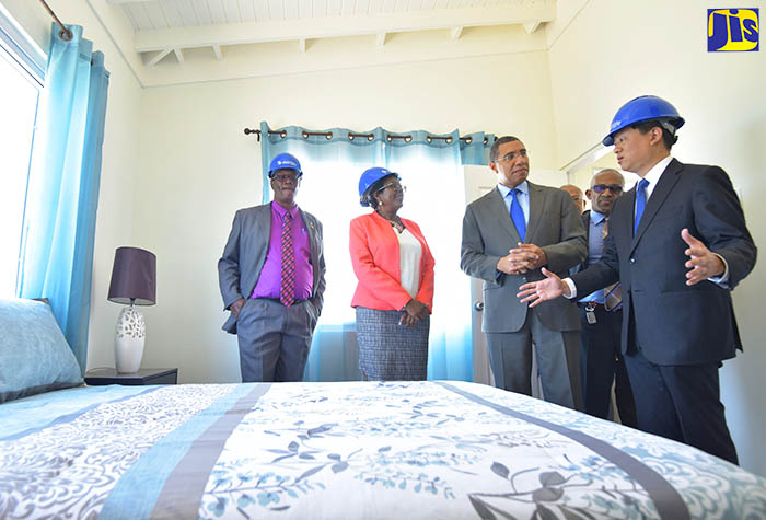 Prime Minister, the Most Hon Andrew Holness (second right), listens as President and Chief Executive Officer (CEO) of World Homes Jamaica Limited, William Lai (right), speaks about the types of amenities being provided through a new housing development being undertaken by his company, as is demonstrated by a model home. The Prime Minister broke ground for the construction of 230 housing units as part of the Foreshore Estate development in Delacree Pen in South West St. Andrew during a ceremony today (April 24). Also pictured (from left) are Councillor for the Greenwich Town Division, Karl Blake; and Member of Parliament for South West St. Andrew, Dr. Angela Brown Burke. In the background is Senior Manager, National Housing Trust (NHT), Donald Moore. World Homes Jamaica is undertaking the new low-income housing development in partnership with the NHT.

