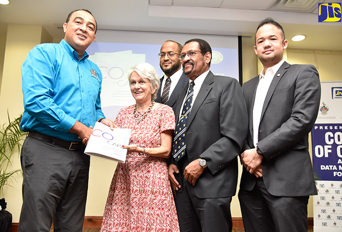 Health Minister, Dr. the Hon. Christopher Tufton (left), is presented with a copy of the Cost of Care and Data Mapping Project Report by Chairperson of the Violence Prevention Alliance (VPA), Dr. Elizabeth Ward, following the document’s launch at the University of the West Indies (UWI) regional headquarters in Mona, St. Andrew. The document was prepared by the VPA in collaboration with the Ministry of Health, University Hospital of the West Indies, Mona GeoInformatics Institute, JN Foundation and the UWI. Sharing the moment (from third left) are: Consultant Anaesthetist, UHWI, Dr. Jason Toppin; Deputy Dean, Faculty of Medical Sciences, UWI, Professor Trevor McCartney; and Director, Mona GeoInformatics Institute, Dr. Parris Lyew-Ayee, Jr.