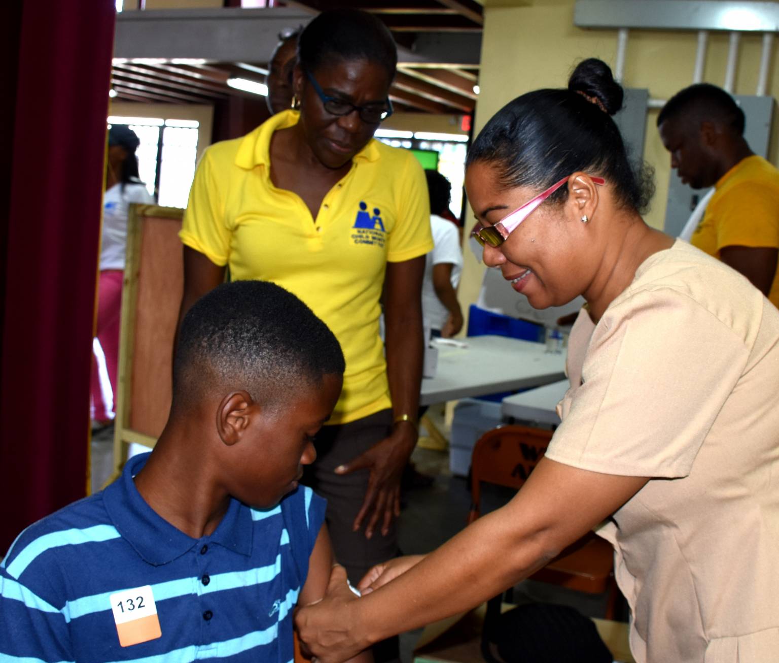 Nurse Andrea James (right) of the Kingston and St. Andrew Health Department, applies pressure to the upper arm of 14-year old Garfield James, after administering a vaccine.  Looking on is NCMC member, Judith Hunter (File).