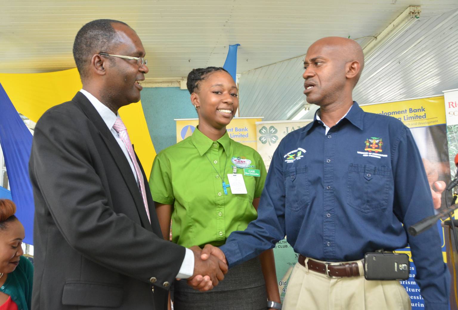 Executive Director of the Jamaica 4-H Clubs, Dr. Ronald Blake (left) shakes hands with Director General in the Ministry of Industry, Commerce, Agriculture and Fisheries, Don McGlashan (right) during the handing over ceremony for the Rio Tinto Alcan Legacy Fund agriculture scholarship programme on December 2 at the Jamaica 4-H Clubs Headquarters in Kingston. Looking on is second year agricultural student at the College of Agriculture, Science and Education and scholarship beneficiary, Ayanna Creary.