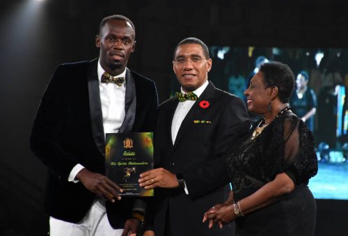 Prime Minister, the Most Hon. Andrew Holness (centre), presents an award to World and Olympic sprint champion, Usain Bolt (left), at a ceremony to honour the 2016 Rio Olympic athletes, at the National Indoor Sports Centre in Kingston, on October 15. Sharing in the moment at (right) is Culture, Gender, Entertainment and Sport Minister, Hon. Olivia Grange.