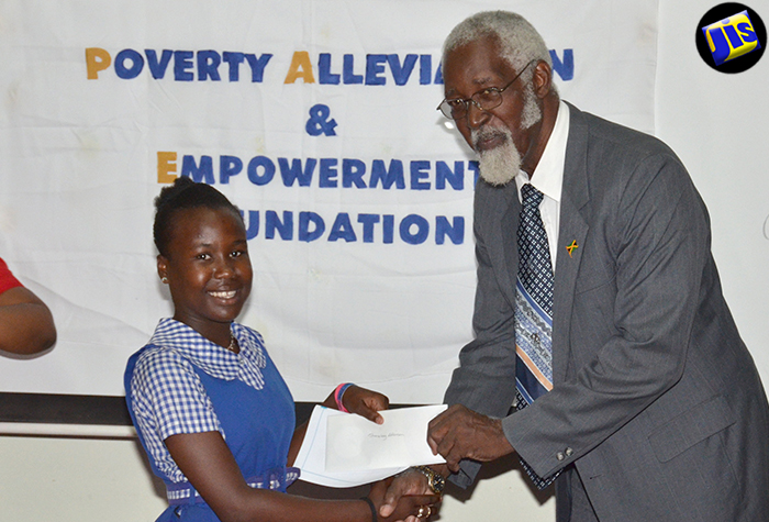 Custos of St. Catherine, Hon. Rev. Jeffrey McKenzie, makes a presentation to Shankay Atkinson, who will be attending the Jonathan Grant High School in September. Occasion was the presentation of grants by the Poverty Alleviation and Empowerment Foundation (PAEF) to nine students from communities in St. Catherine. The ceremony was held on August 3 at the Social Development Commission’s (SDC) offices in Spanish Town. 