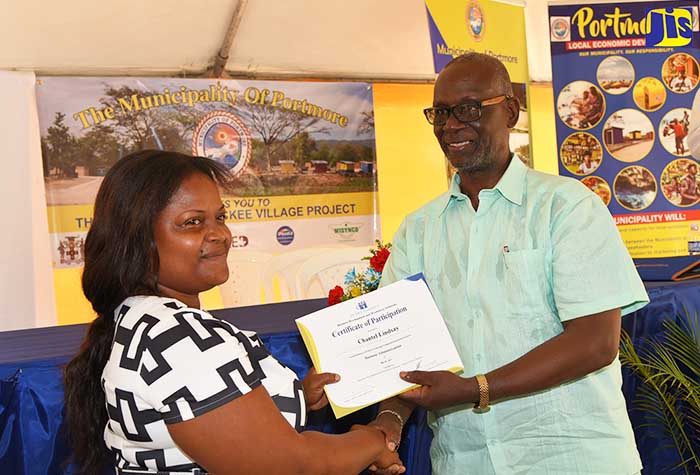 Minister of Local Government and Community Development, Hon. Desmond McKenzie (right), presents Ackee Village vendor, Chantel Lindsay, with a HEART Trust/NTA certificate for successfully completing a customer service training programme. The presentation was made prior to the launch of the market located along the Dyke Road in Portmore in July.