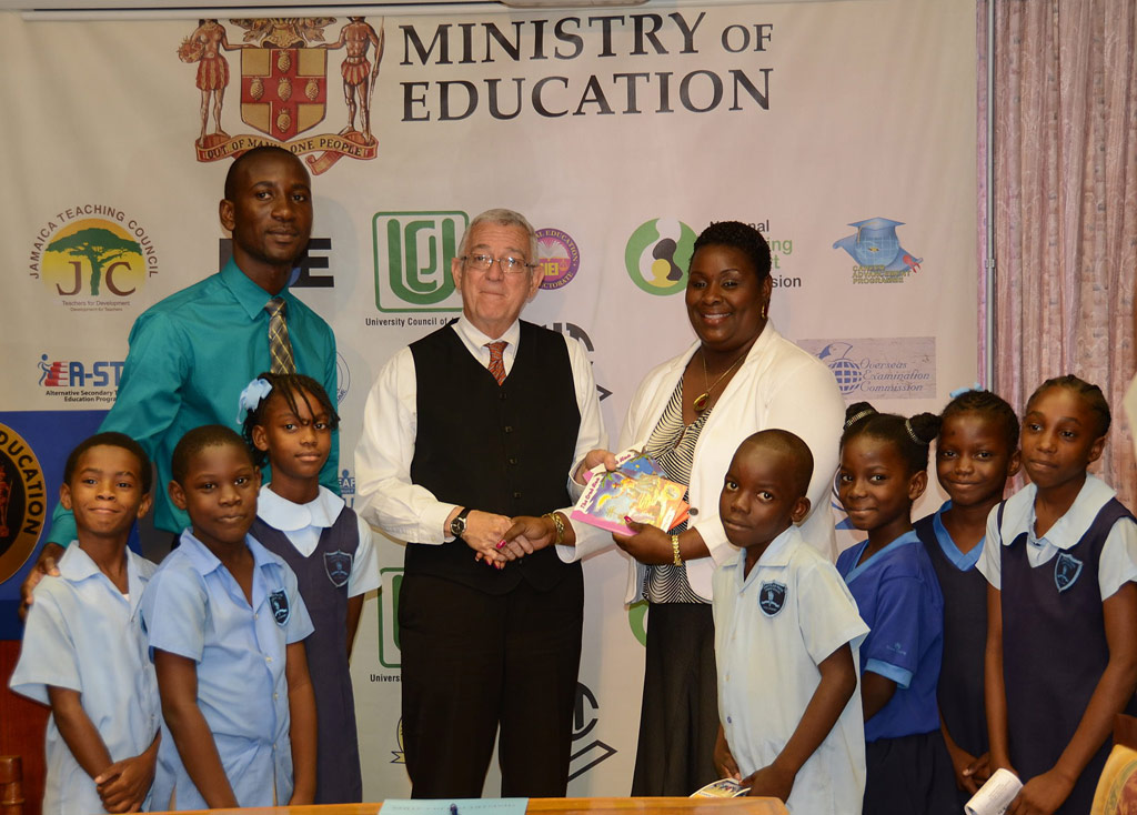 Minister of Education, Hon. Rev. Ronald Thwaites (centre), accepts school supplies from Company Director, Kingston Bookshop, Damani Johnson (right), during Wednesday’s (July 3) official launch of Camp Summer Plus 2013, at the Ministry’s Heroes Circle offices in Kingston. Others sharing the moment are: Principal of Chetolah Park Primary, Robert Smith, and students at the institution.