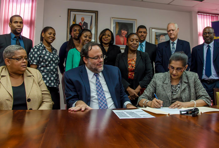 Administrator-General & CEO of the Administrator General’s Department  Lona Brown (Front left) signs the first two Instruments of Administration to be processed  following recent amendments to the Administrator General’s Act  at the Offices of the Administrator General’s Department on Friday October 2 . Looking on are front row : Permanent Secretary in the Ministry of Justice Mrs Carol Palmer and Minister of Justice Hon. Mark Golding.  
Back row: Legal Officer - Allan Hunter; Legal Secretary -  Janice Brimm; Legal Secretary  - Sherene Hibbert; Legal Officer  - Kedia Delahaye; Estate Administration Executive - Ingrid Cole; Legal Officer  - Geraldine Bradford; Human Resource & Administration Executive - Colin Ebanks; Deputy Administrator-General - Andrew Gyles and Finance & Planning Executive - Patrick Wright. 
