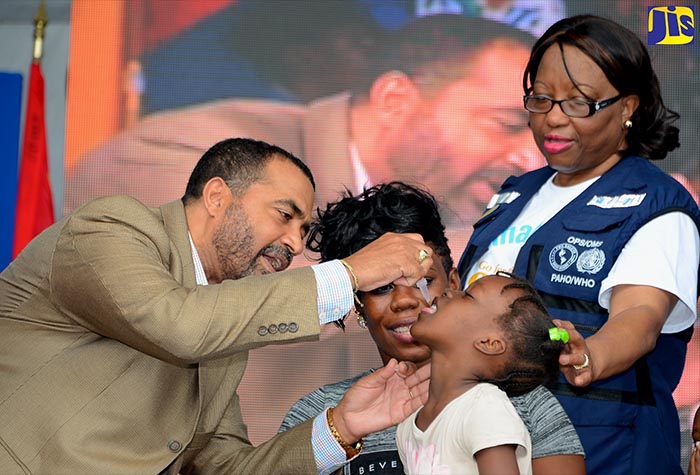 Then Acting Chief Medical Officer in the Ministry of Health, Dr. Winston De La Haye (left), administers polio drops to young Mickayla Edwards, during the official launch of the 14th Vaccination Week in the Americas at Emancipation Park in New Kingston on April 23. Observing the procedure (from right) are Director of the Pan American Health Organization (PAHO), Dr. Carissa F. Etienne, and Mickayla’s mother, Carla Peart. Vaccination Week in the Americas is marked annually during the last week of April and is used to promote the benefits of vaccination. 