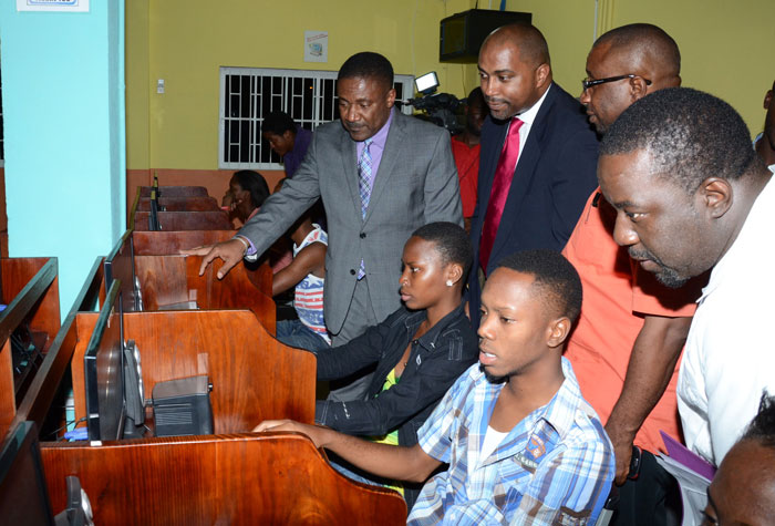 Minister of Science, Technology, Energy and Mining, Hon. Phillip Paulwell (left) observes as members of the McGregor Gardens community, (seated from left), Nyoka Senior and Shaquille Watson, utilize computers at the McGregor GardensCommunity Cyber Vision Cafe in Kingston. The facility was officially opened during a ceremony on April 23. Also looking on (standing from second left) are: State Minister in the Science Ministry, Hon. Julian Robinson; Deputy Mayor of Kingston, Councillor Andrew Swaby; and Chairperson for the event, Ricardo Bennett. 