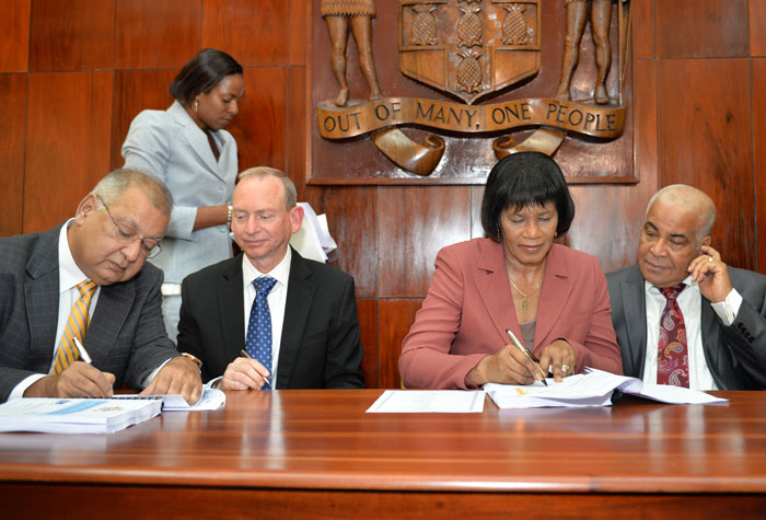 Prime Minister, the Most Hon. Portia Simpson Miller (2nd right); and Chairman, National Water Commission (NWC), Prakash Vaswani (left), sign the contract for the $4.9 billion Non-Revenue Water Reduction Co-Management project, during a ceremony  at the Office of the Prime Minister in Kingston today (July 8). Chairman of Israeli-based company Miya, Meir Wietchner (2nd left); and Minister of Water, Land, Environment and Climate Change, Hon. Robert Pickersgill, look on.