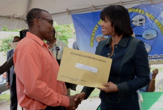 Local Government and Community Development Minister and Member of Parliament, South West Clarendon, Hon. Noel Arscott (left), presents Anjella Beezer of the Ebony Park Housing Scheme, Toll Gate, Clarendon, with her property title during the presentation ceremony in the community on October 11. Mrs. Beezer is one of some 70 persons who received titles after a 30-year wait.