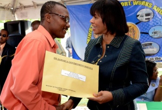 Prime Minister the Most Hon. Portia Simpson Miller (right), presents a title to Leon George, one of approximately 70 persons from the Ebony Park Housing Scheme in Clarendon to receive titles at a ceremony, held on October 11 in the community.