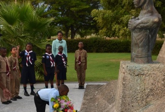 Outstanding student of Free Town Primary School, nine year-old Jaiden Morrison, places flowers at the shrine of National Hero, the Right Excellent Paul Bogle, at this year’s  ‘Salute to the National Heroes’,  held on National Heroes Day (October 21), at the National Heroes Park in Kingston. Looking on are Vice Principal of Half-Way Tree Primary, Shelley Lee, and 
 students and  Cub Scouts of Half-WayTree Primary.