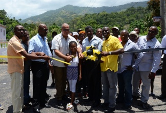 State Minister in the Ministry of Transport, Works and Housing, Hon. Richard Azan (4th left), is assisted by nine-year old Sherona Ferguson (5th left), of Enfield, St. Mary, to cut the symbolic ribbon to officially re-open the newly rehabilitated Enfield main road on July 17. The three-month project,  implemented by the National Works Agency (NWA), was financed by the Ministry at a cost of $92 million. Others sharing in the occasion are: NWA Chief Executive Officer, E.G. Hunter (3rd left); Member of Parliament for South East St Mary, where the road is located, Dr. Winston Green (4th right); and NWA Communications and Customer Service Manager, Stephen Shaw (3rd right).
