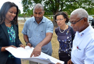 Minister of State in the Ministry of Science, Technology, Energy and Mining, Hon. Julian Robinson (second left); along with Project Engineer, Michael Hemmings (right); President of the Rotary Club of Kingston, Allison Peart (second right); and President of Junior Achievement Jamaica (JAJ), Alphie Mullings-Aiken, examine the plan for the Junior Achievement (JA) BizTown, during the ground breaking ceremony for the project held on Friday (January 17), at the Ministry of Education’s Caenwood Centre complex in Kingston.