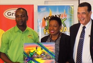 Culture, Gender, Entertainment and Sport Minister, Hon.  Olivia Grange (centre), is presented with artwork depicting local scenery, by Chief organiser of the 2017 MoBay Jerk Fest, John Lindo (left), after she addressed the launch of the event on July 5 at the Royal Decameron Resort in St. James. Sharing the moment is Montego Bay's Mayor, Councillor Homer Davis. The jerk festival is to be held on August 1 at the Catherine Hall Entertainment Centre .