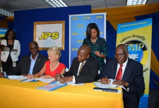 State Minister in the Ministry of National Security, Senator the Hon. Pearnel Charles (Jr.) (2nd right) and  President and Chief Executive Officer of JPS Co., Kelly Tomblin (2nd left), signs  Memorandum of Understanding to provide internship opportunities for 45 at-risk youth from Citizen Security and Justice Programme (CSJP) target communities. Witnessing  are Vice President of Customer Service and Communications at JPS Co., Keith Garvey (left) and Project Manager for CSJP, Simeon Robinson (right). Looking on are Programme Manager of the Community Renewal and Customer Solution Department, Marilyn McDonald (right, standing), and Corporate Communications Officer at JPS Co., Audrey Williams (left, standing).