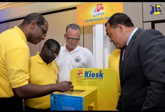 Health Minister, Dr. the Hon Christopher Tufton (right), observes as the National Health Fund’s (NHF) Senior Vice President for Information and Communications Technology, Granville Gayle (left), demonstrates how the NHF’s newly launched ‘Quick Prescript’ mobile application can be accessed via kiosks that will be installed at several locations islandwide, following the launch at the Spanish Court Hotel, New Kingston, on Tuesday (April 24). Looking on (from second left) are NHF Chief Executive Officer, Everton Anderson; and Chairman, Gregory Mair.