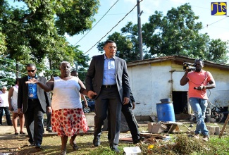 Prime Minister, the Most Hon. Andrew Holness (right), is escorted into the backyard at the home of Central Clarendon resident, Stephanie Largie (left), during a tour on May 5 of sections of constituency that were flooded by heavy rains in April.