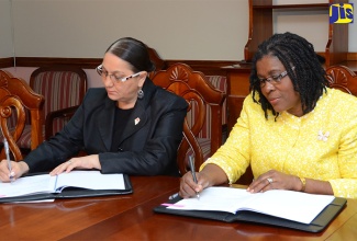 Permanent Secretary in the Ministry of Economic Growth and Job Creation, Mrs. Audrey Sewell (right) and Acting Principal Director of Technical Services at the Rural Agricultural Development Authority (RADA), Marina Young, sign a Memorandum of Understanding (MOU), yesterday (October 20), at the Ministry’s New Kingston offices, for a project geared at enabling farmers and other groups working in tourism to lessen the impacts of climate change, through a US$17-million Adaptation Fund.