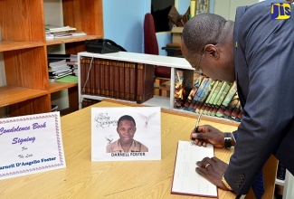 Minister of Education, Youth and Information, Senator the Hon. Ruel Reid, signs a condolence book for Mona High School student, Darnell Foster, at a special devotion at the school on Thursday, January 26. Darnell died suddenly on Monday (January 23) after collapsing in Half-Way Tree.
 
