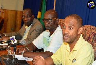 Education, Youth and Information Minister, Senator the Hon. Ruel Reid (left), and Local Government and Community Development Minister, Hon. Desmond McKenzie, listen as Director of the Meteorological Service Division in the Ministry of Economic Growth and Job Creation, Evan Thompson, addresses journalists, during Monday’s (August 1) media briefing at the Office of the Prime Minister (OPM).