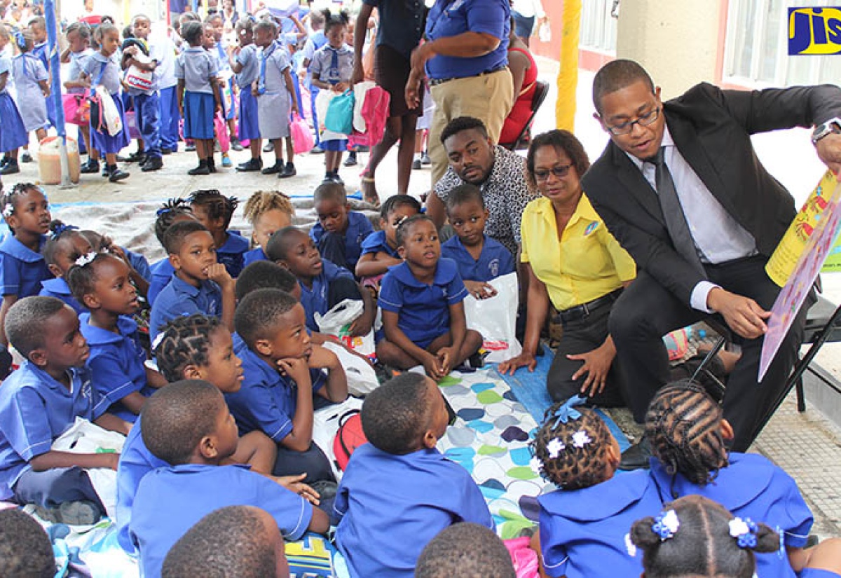 Minister of State in the Ministry of Education, Youth and Information, Hon. Floyd Green (right), reads to children attending the Early Childhood Commission’s (ECC) ‘Read Pon Di Cawna’ event held recently at Orange Park, downtown Kingston. Seated next to Mr. Green is Executive Director of the ECC, Karlene DeGrasse-Deslandes.

