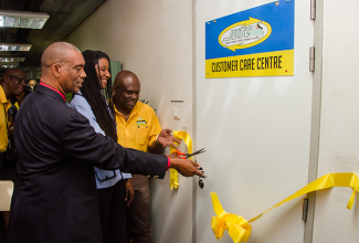 Chairman of the Jamaica Urban Transit Company (JUTC), Dr. Garnett Roper (left); and Managing Director, JUTC, Colin Campbell (right), assist Senior Director (Acting) of the Modernization Programme Implementation Unit, Office of the Cabinet, Michele Gordon-Somers, in cutting the ribbon to officially open the JUTC’s Customer Care Centre at the Half-Way-Tree Transport Centre on November 5. 