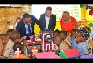 Managing Director of the Jamaica Social Investment Fund (JSIF), Omar Sweeney (left), admires a model fire station during a walk-through of the reconstructed St. Paul Early Childhood Institution in Kingston on July 7. Head of Operations for the EU Delegation to Jamaica, Achim Schaffert (centre); widow of founder of the school, Viola Gibson, and students of the school, also look on. The institution was rebuilt at a cost of $45.3 million under the EU-funded Poverty Reduction Programme (PRP-IV).