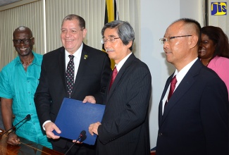 Finance and the Public Service Minister, Hon. Audley Shaw (2nd left), and Japan’s Ambassador to Jamaica, His Excellency Masanori Nakano (2nd right), display signed copies of a grant agreement for the provision of J$1.6 billion (¥1.39 billion/US$12.58 million) by the Government of Japan to fund the implementation of Jamaica’s ‘Improvement of Emergency Communication System Project’. The signing took place at the Ministry’s National Heroes Circle offices in Kingston on Thursday, April 6. The project will be implemented by the Office of Disaster Preparedness and Emergency Management (ODPEM). Looking on (from left) are: Local Government and Community Development Minister, Hon. Desmond McKenzie, who has portfolio responsibility for ODPEM; and Japan International Cooperation Agency (JICA) Resident Representative in Jamaica, Kenji Tobita. In the background is the Ministry’s Senior Director for Negotiations, Nadine James.