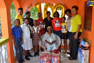 Centenarian, Merinda ‘Miss Mim’ Bryan is surrounded by students and teachers of the John Rollins Success Primary School after they presented her with gifts during a visit to her home in Barrett Town, St. James, on December 18. 