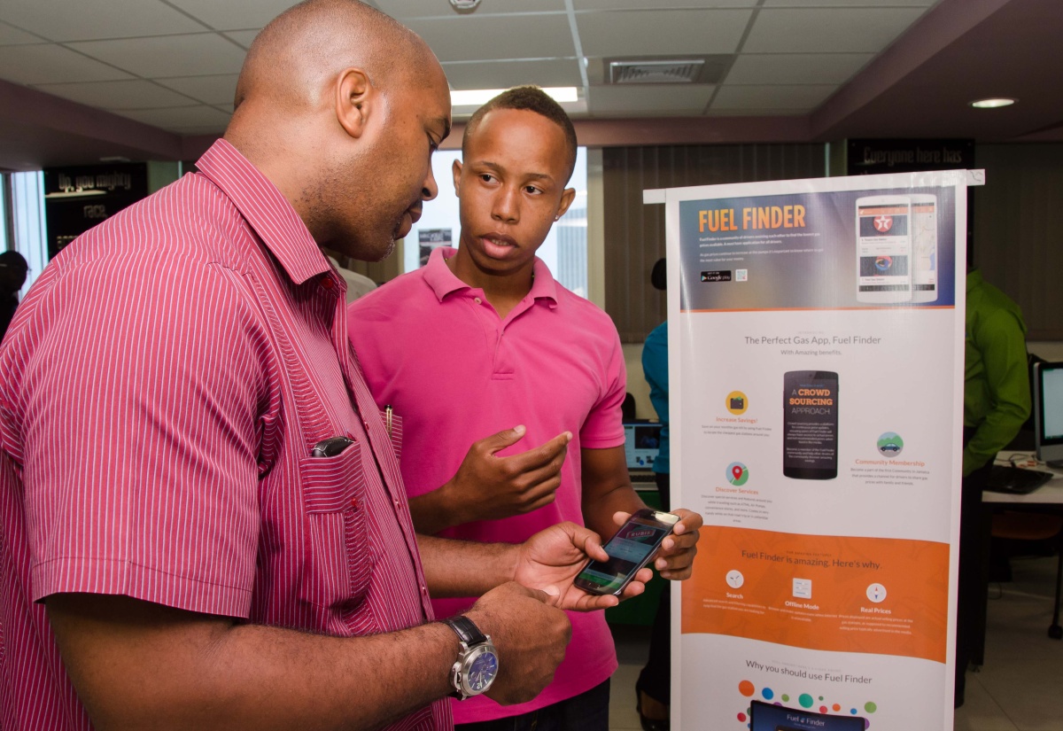 Minister of State in the Ministry of Science, Technology, Energy and Mining, Hon. Julian Robinson (left), tries out the ‘Fuel Finder’ application developed by young technology entrepreneur, Garfield Coke. The app, which lists gas stations in the island, and quotes prices, services offered, among other things, was recently showcased at a Start-up Jamaica exposition held in Kingston. 