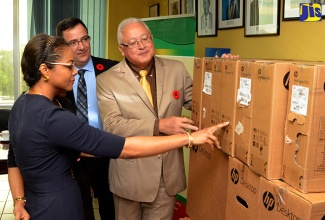 Justice Minister, Hon. Delroy Chuck (right) and Attorney General (AG), Hon. Marlene Malahoo Forte (left), peruse the specifications of one of the 25 computers provided to the AG’s Department by the Government of Canada. The computers, along with backup storage devices and a projector, were handed over by Canadian High Commissioner to Jamaica, His Excellency Sylvain Fabí (centre), during a ceremony at the AG’s Office in New Kingston. 