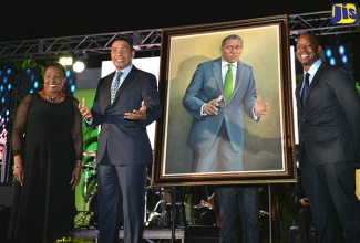 Prime Minister, the Most Hon. Andrew Holness (2nd left) replicates the pose he holds in his portrait painted by artist Kai Watson (right), which was unveiled during the media launch of ‘Jamaica 55’ Independence celebrations on the lawns of Jamaica House on Wednesday (April 5). At left is Minister of Culture, Gender, Entertainment and Sport, Hon. Olivia Grange. The painting is one of three that Mr. Watson has been commissioned to complete as part of the Legacy Projects Programme for ‘Jamaica 55’. Portraits of former Prime Ministers, the Most Hon. Portia Simpson Miller; and Hon. Bruce Golding are also to be painted. Mr. Holness’ portrait will join those of previous Prime Ministers, which adorn the walls of the Cabinet room at Jamaica House. 
