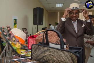 Minister of Tourism, Hon. Edmund Bartlett, fits a hat at the Craft Enhancement Project Recognition and Awards Ceremony, held on July 12, at the New Kingston Business Centre.