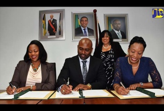 Minister of Science, Energy and Technology, Dr. the Hon. Andrew Wheatley (centre) along with representatives from telecommunications companies Digicel and Flow, sign an agreement that will allow free access to all government websites. The representatives (seated from left) are Legal and Regulatory Director, Digicel, Maia Wilson; and Vice President, Legal and Regulatory, Flow, Rochelle Cameron. The signing took place during a ceremony at the Energy Ministry’s Trafalgar Road offices in New Kingston, today (March 15). Overseeing the proceedings is Permanent Secretary in the Ministry, Hilary Alexander.